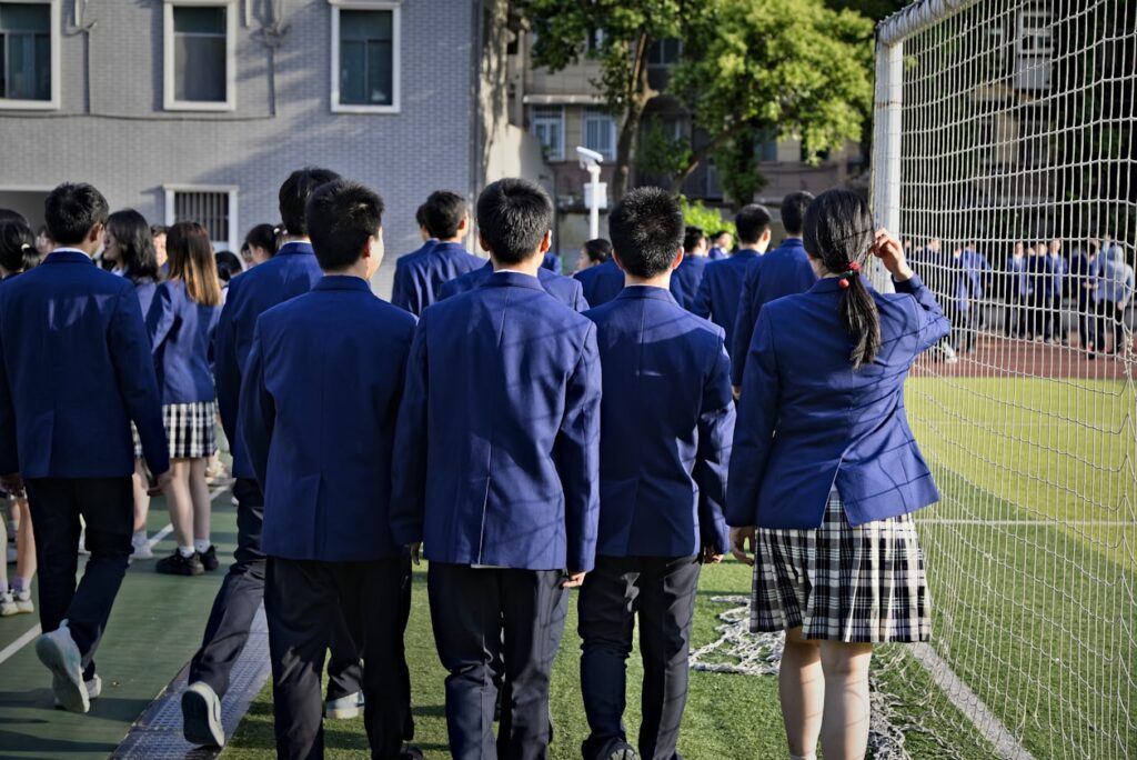 Students in uniform are walking near a sports field.